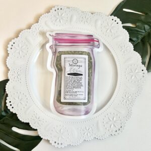 Blooming with Joy Moringa Loose Herb Superfood in mason jar pouch on decorative plate with Monstera leaf